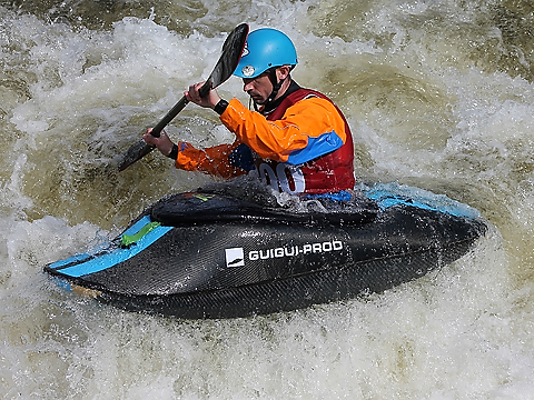 paddler in orange gear, in black and blue canoe, with black paddle, tackling the rapids