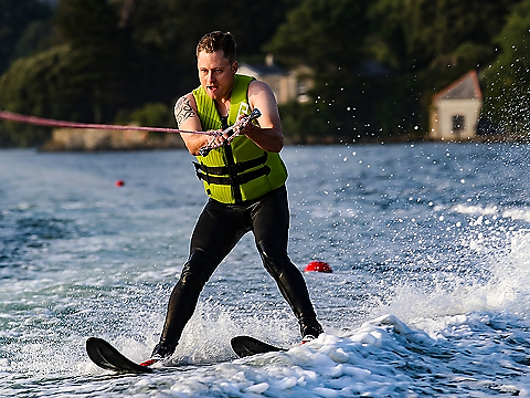 Novice water skier in high-vis safety jacket concentrating hard on staying upright on water